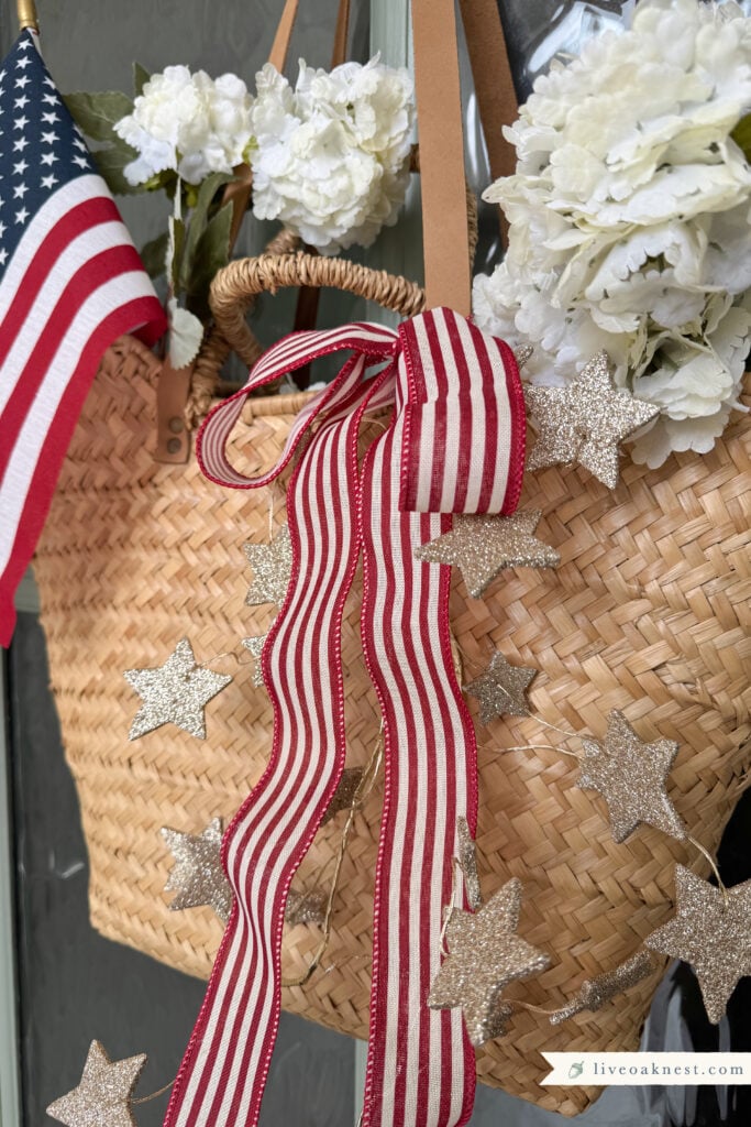 Patriotic Front Door Decor That Feels Cozy & Timeless, Basket of flowers on front door, glitter star garland, patriotic porch ideas, porch decor from Live Oak Nest www.liveoaknest.com