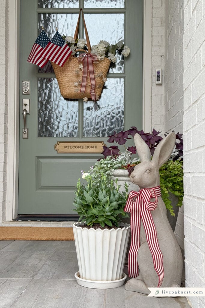 Timeless Patriotic Decor on Small Front Porch. Basket with White Flowers and American Flag. Standing Porch Bunny with Red and White Ribbon